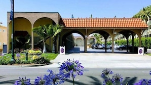 A building with a red-tiled roof, arched entrances, and a landscaped area with flowers. - Kings Inn Anaheim (Anaheim)