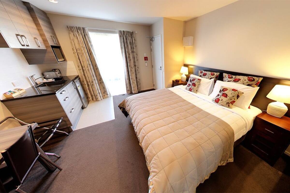 A hotel room with a bed, bedside tables, a desk, and a kitchenette.