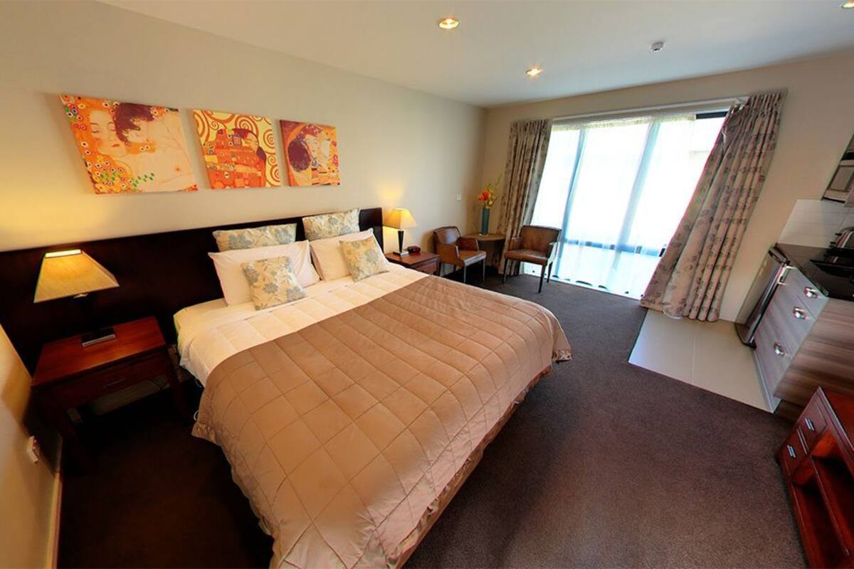 A hotel room with a large bed, a desk, a chair, a small table, and a window with curtains.