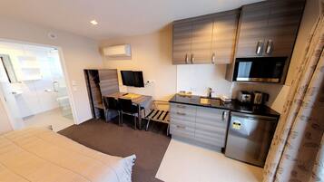 Une chambre d’hôtel compacte comprenant un lit, un bureau avec une chaise, une kitchenette et une salle de bain avec douche.