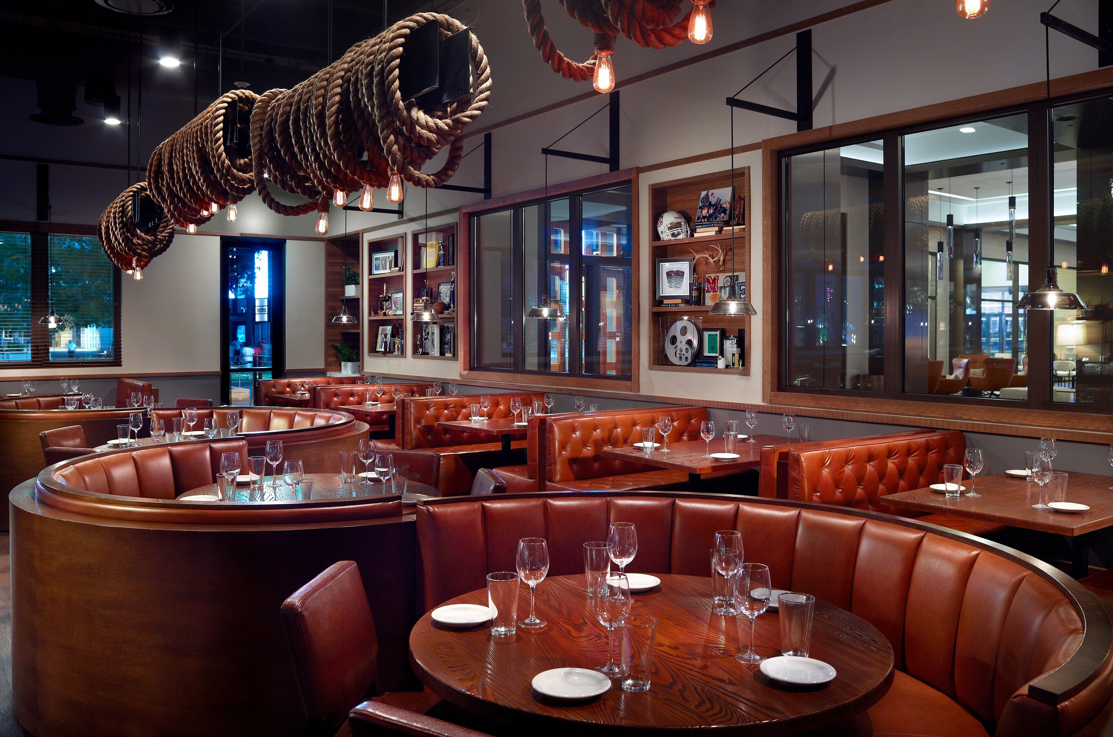 Een restaurant met lederen banken, houten tafels en hanglampen.