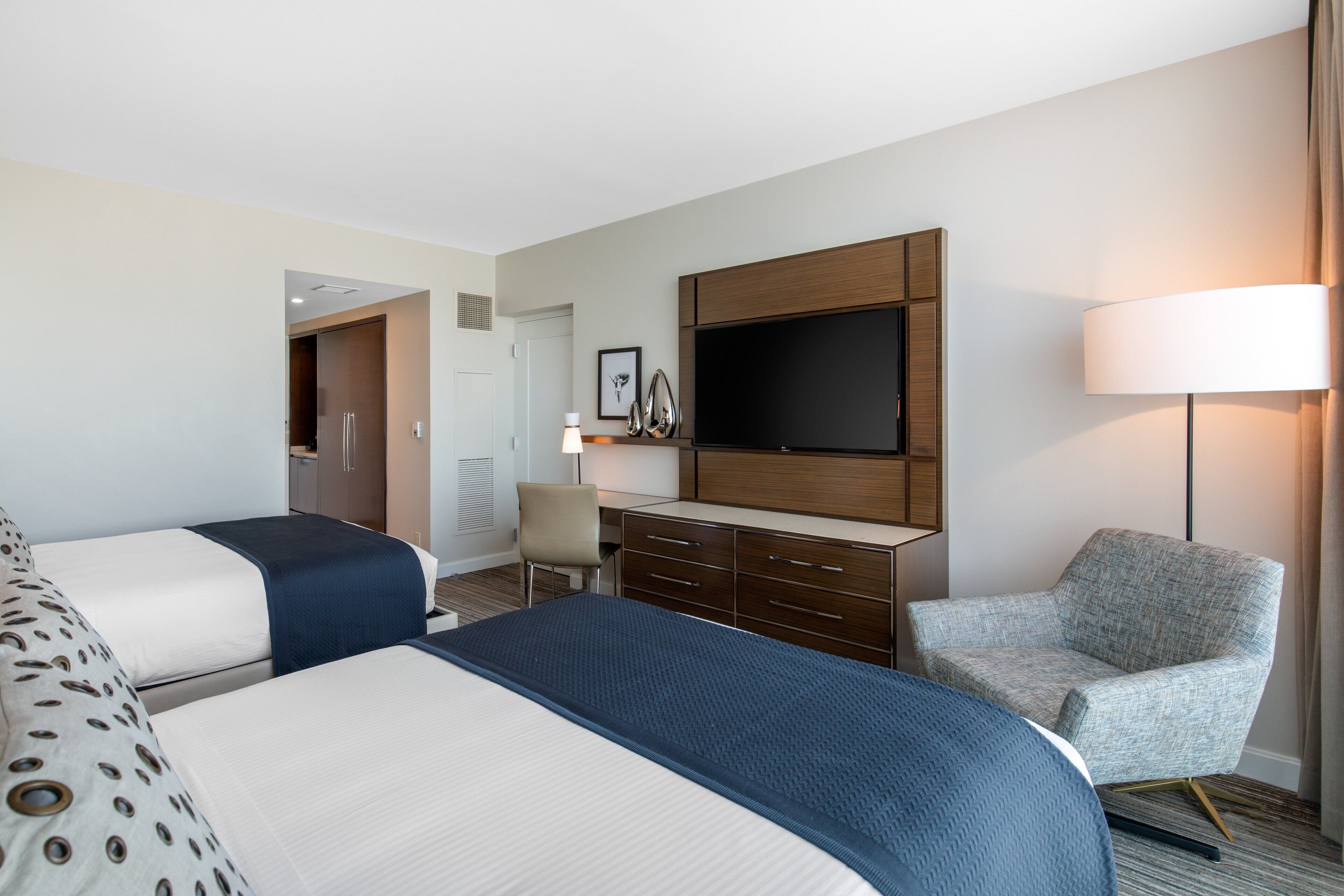 Une chambre d’hôtel avec deux lits, un bureau, une chaise, une télévision et une lampe.
