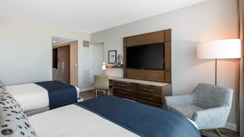 Une chambre d’hôtel avec deux lits, un bureau, une chaise, une télévision et une lampe.