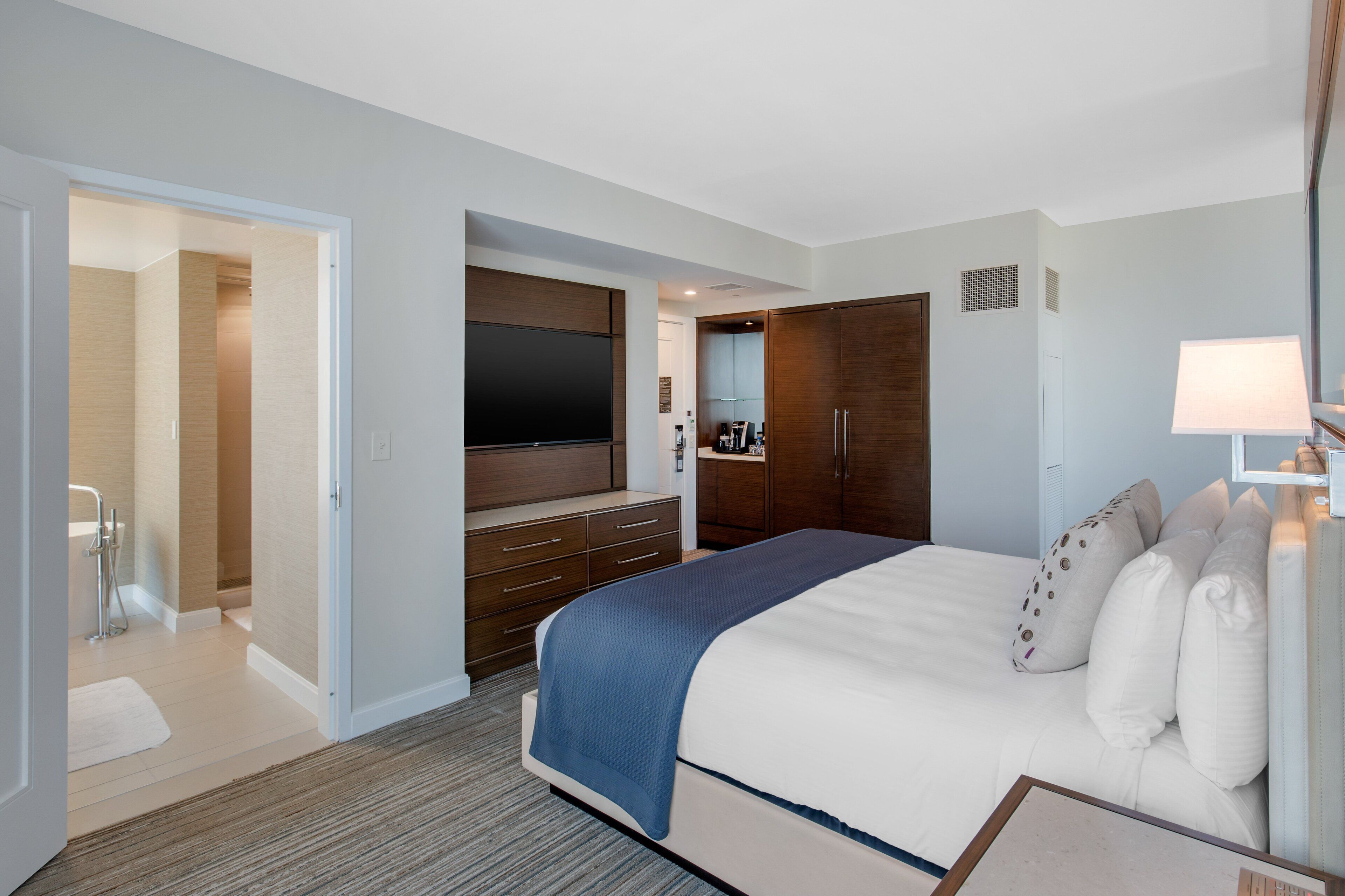 A hotel room with a large bed, a TV, wooden wardrobe, and a bathroom visible through an open door.
