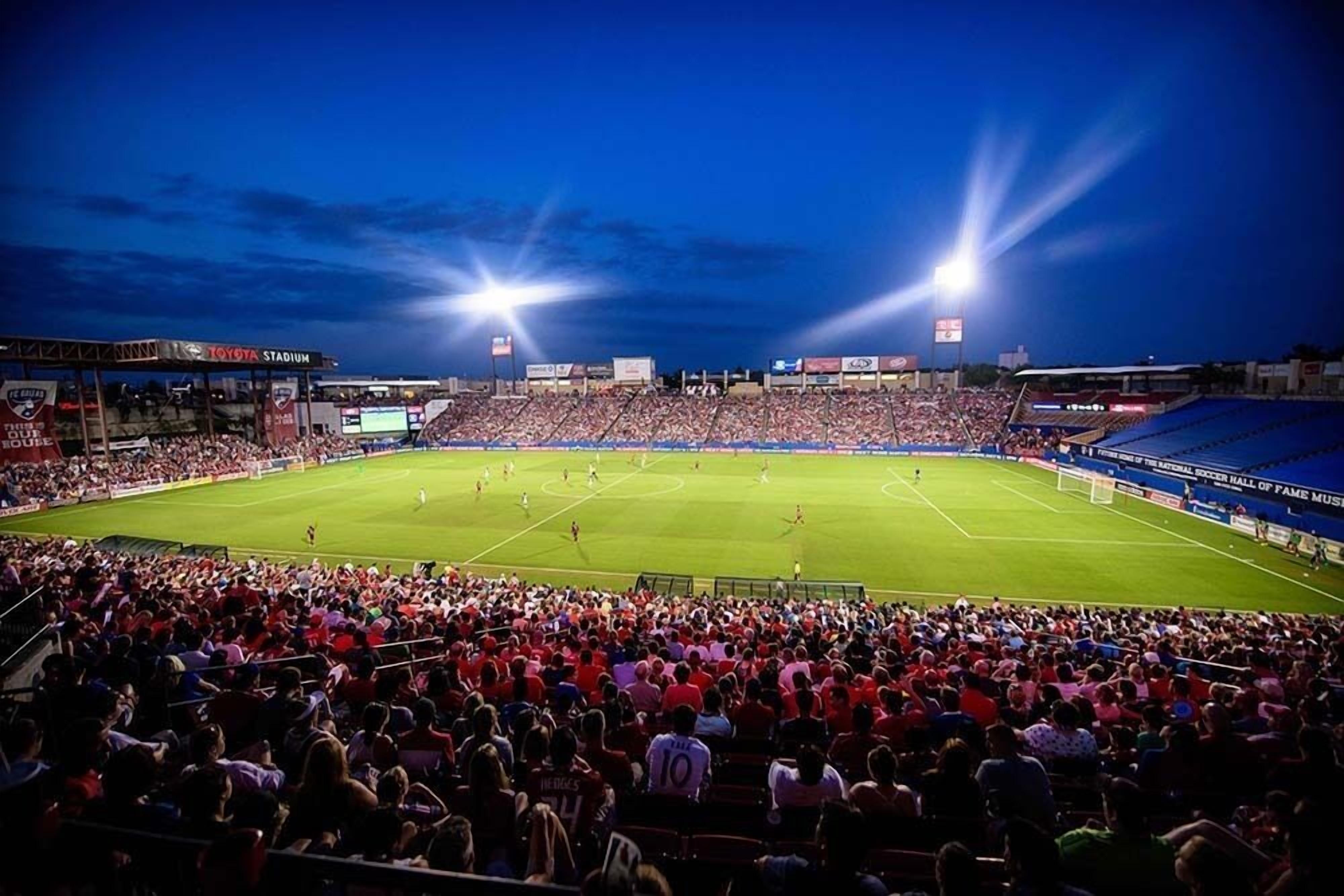 A stadium with multiple soccer fields, large seating capacity, and bright floodlights.