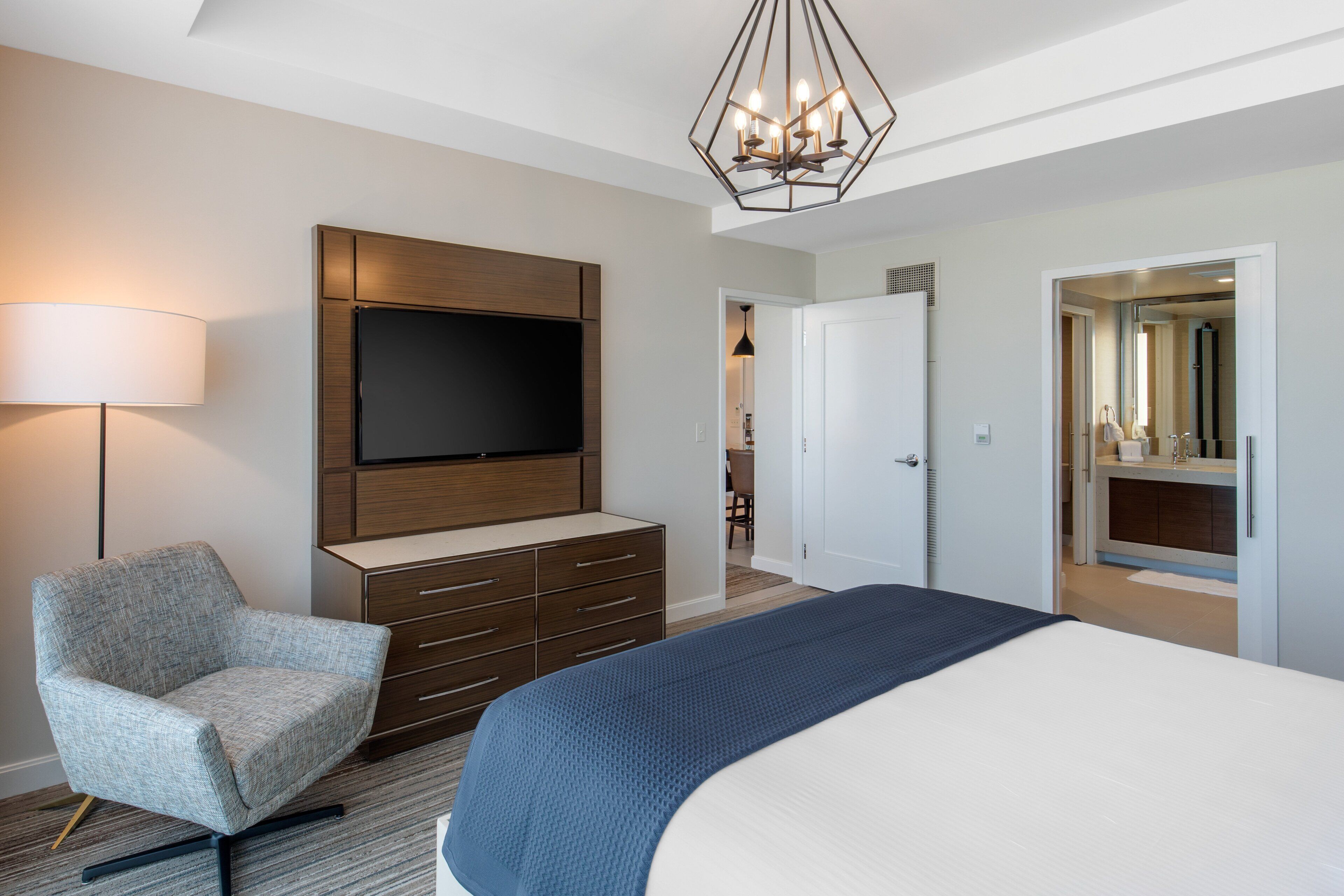 Una habitación de hotel moderna con una cama grande, un televisor de pantalla plana montado en un mueble de madera, una silla y un escritorio.