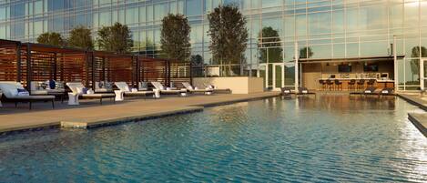 A modern hotel pool area with lounge chairs and a bar.