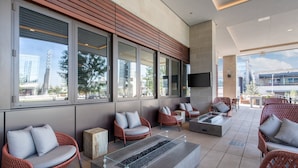A modern outdoor seating area with wicker chairs, a fire feature, and large windows offering views of the city. - Omni Frisco Hotel at The Star (Frisco)