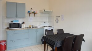 A compact kitchen with a microwave, stove, and sink. There is a dining table with chairs and a red trash bin. - Private Bay House (Wellington)