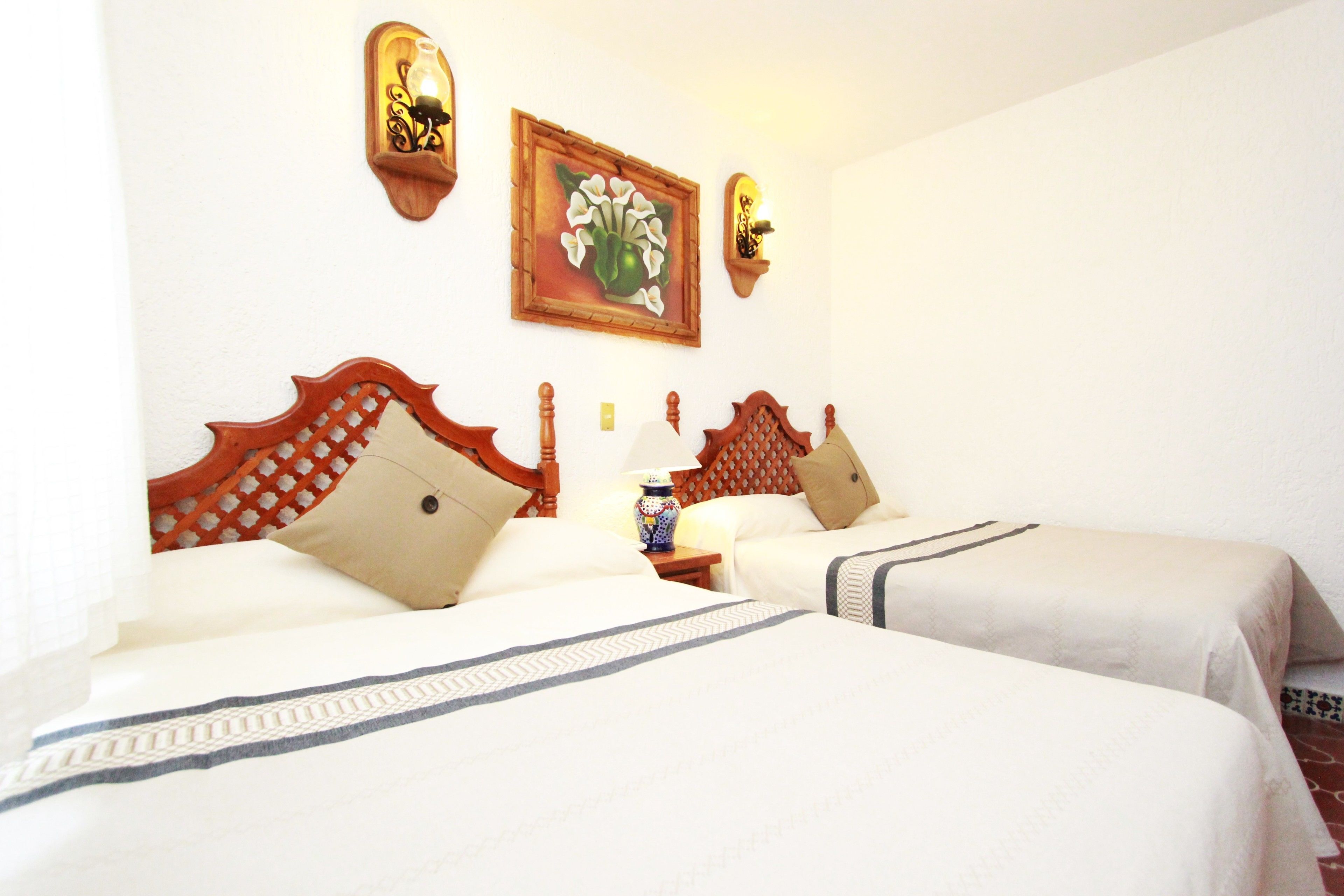 A hotel room with two beds, wooden headboards, white bedding, and decorative wall sconces.