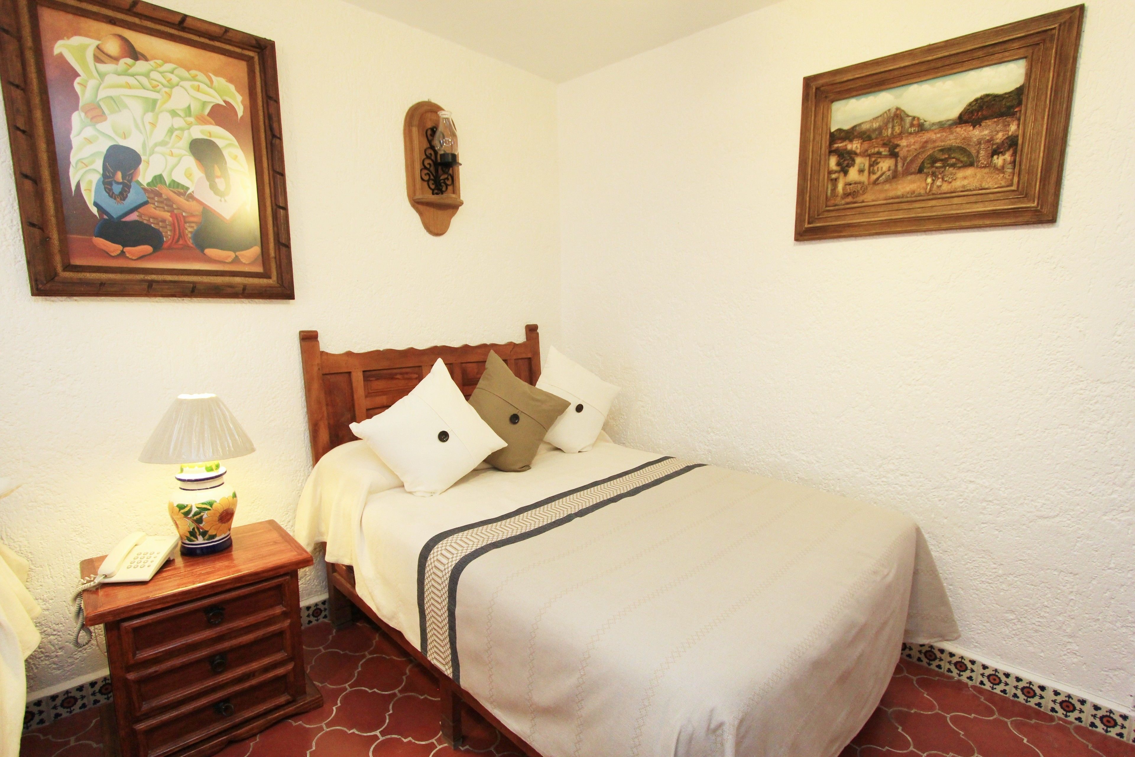 A neatly made bed with a wooden headboard, a bedside table with a lamp, and two framed artworks on the walls.