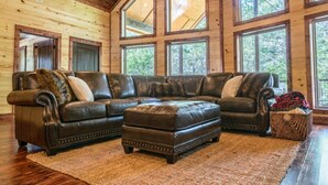 A large L-shaped sectional sofa with matching ottoman, positioned on a wooden floor with a large window in the background.