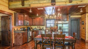 A rustic kitchen with wooden cabinets, a dining table with chairs, and a chandelier.