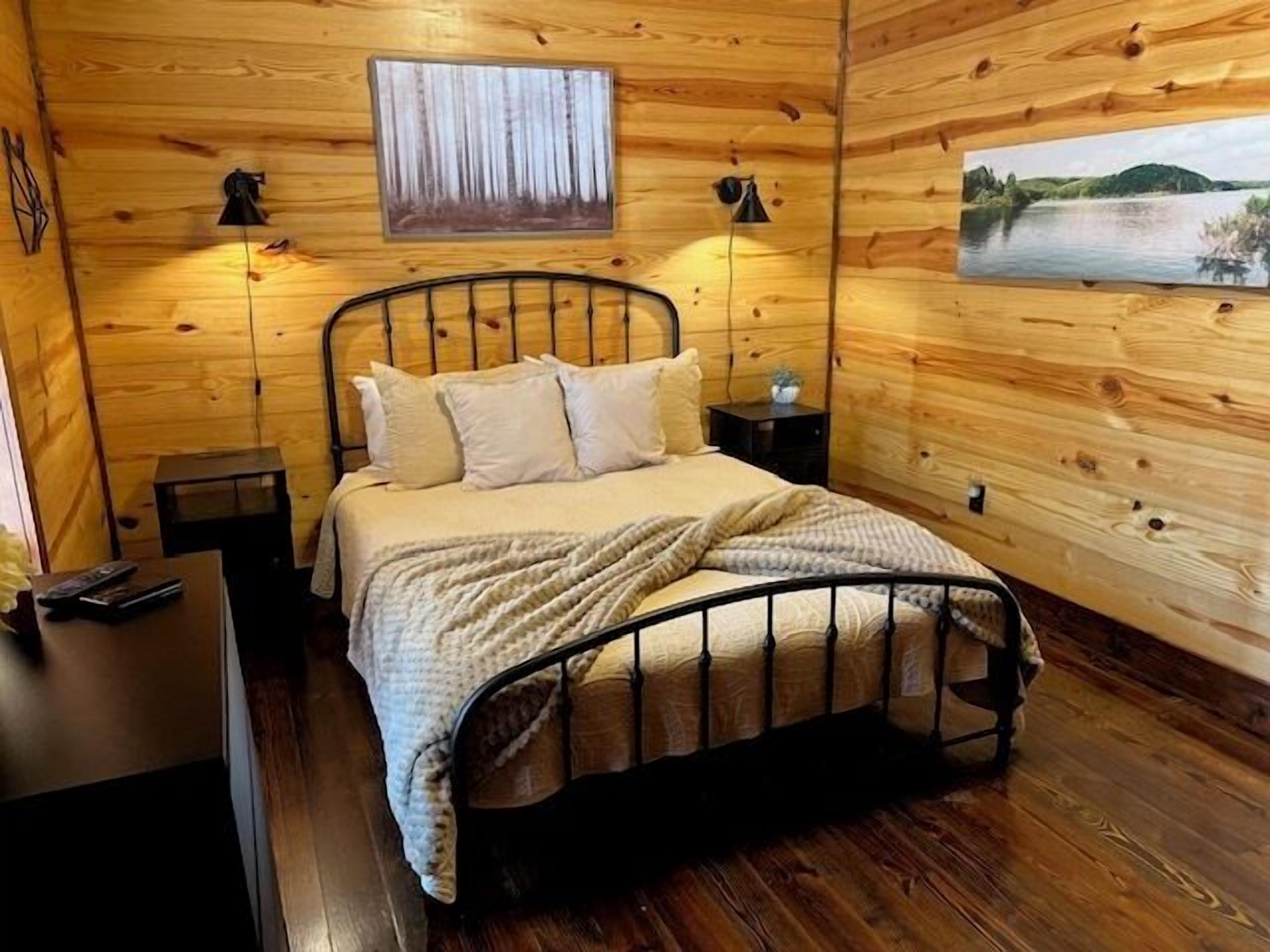 Un dormitorio de cabaña de madera acogedor, con una estructura de cama de metal, una mesita de noche y un velador.