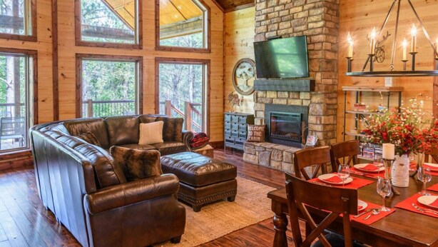 A cozy cabin interior with a stone fireplace, leather sofa, and large windows.