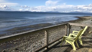 Une plage avec une terrasse en bois, une rambarde en métal et deux chaises en plastique jaunes.
