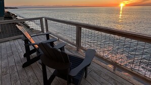 Une terrasse avec des chaises en bois et une table, donnant sur une étendue d’eau au coucher du soleil.