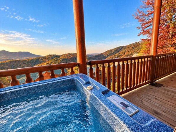 A hot tub on a wooden deck with a view of a mountainous landscape.