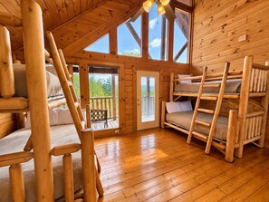A cabin interior with a wooden floor, bunk beds, a staircase, and a balcony with a view. - Mountain Views + Theater, Game Room & Hot Tub - Free Daily Activities (Sevierville)