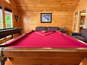 A pool table with balls, a framed picture on the wall, and a brown leather couch.