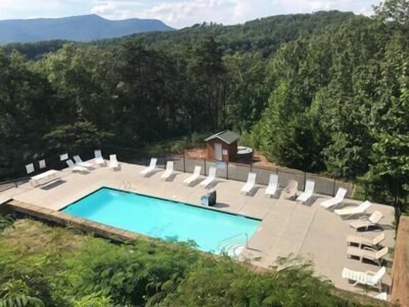 Una piscina con sillas de descanso y un pequeño edificio, rodeado de un bosque denso y montañas.