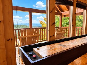 A wooden deck with a shuffleboard table, chairs, and a view of a mountainous landscape. - Mountain Views + Theater, Game Room & Hot Tub - Free Daily Activities (Sevierville)