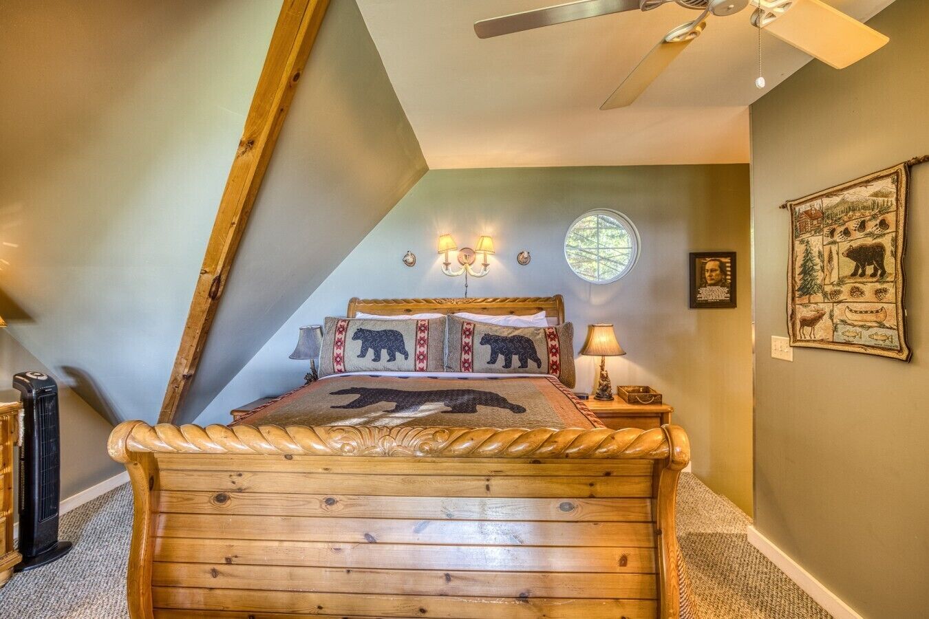 A bedroom with a sloped ceiling, a bed with a bear-themed bedspread, a round window, and a wall-mounted picture.