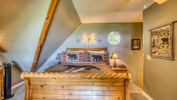 A bedroom with a sloped ceiling, a bed with a bear-themed bedspread, a round window, and a wall-mounted picture.