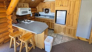 Cocina de cabaña de troncos con armarios de madera, una isla central con taburetes, un microondas, un refrigerador y una lámpara en el techo.