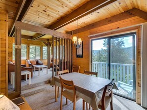 A wooden cabin interior with a dining table, chairs, a sofa, and a balcony with a railing. - Crow`s Nest - Fun Treetop Design (Leavenworth)