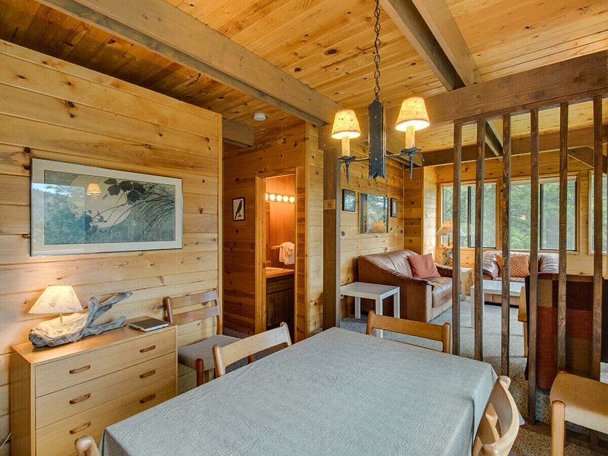 L’intérieur d’un chalet en bois comprend une table à manger, des chaises, un canapé et une petite table avec une lampe.