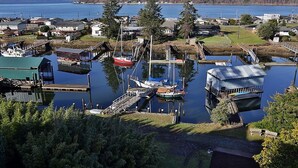 Un puerto deportivo con barcos amarrados, un pequeño edificio y una colina boscosa al fondo.