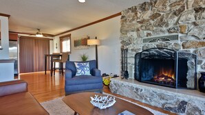 Una sala de estar con chimenea de piedra, un sofá, una mesa de centro y un comedor al fondo.
