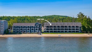 Ein Hotel am Wasser mit mehreren Etagen und Balkonen, nahe einem Strand und einem bewaldeten Gebiet.