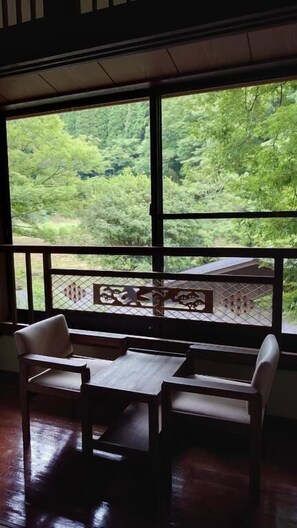 A room with a table and chairs facing a large window with a view of a forest. - Kurokawa Onsen Ryokan Ichinoi (Minamioguni)