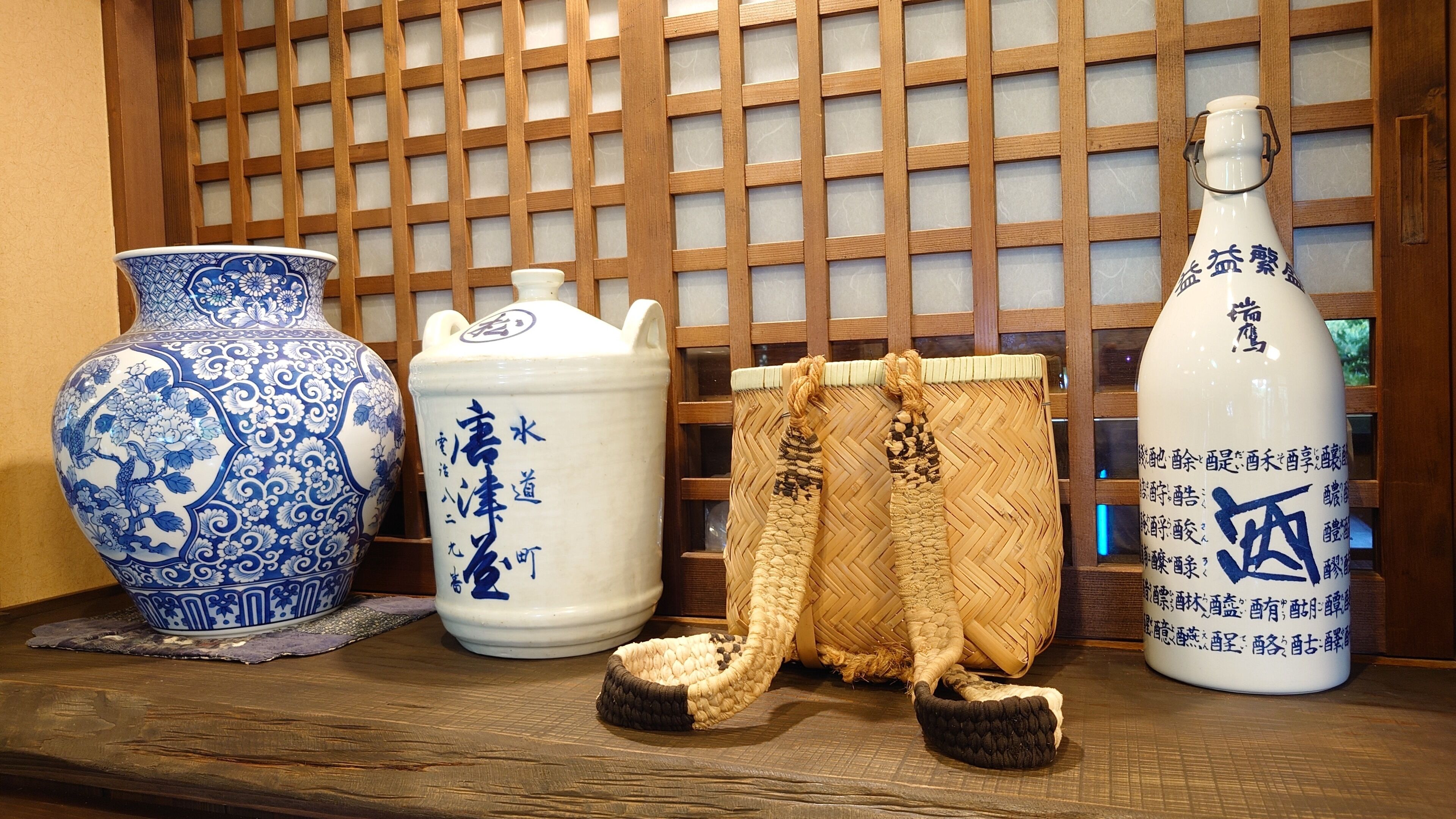 A display of traditional Japanese ceramics and textiles, including a blue and white vase, a white ceramic pitcher, and a woven basket with a rope handle.