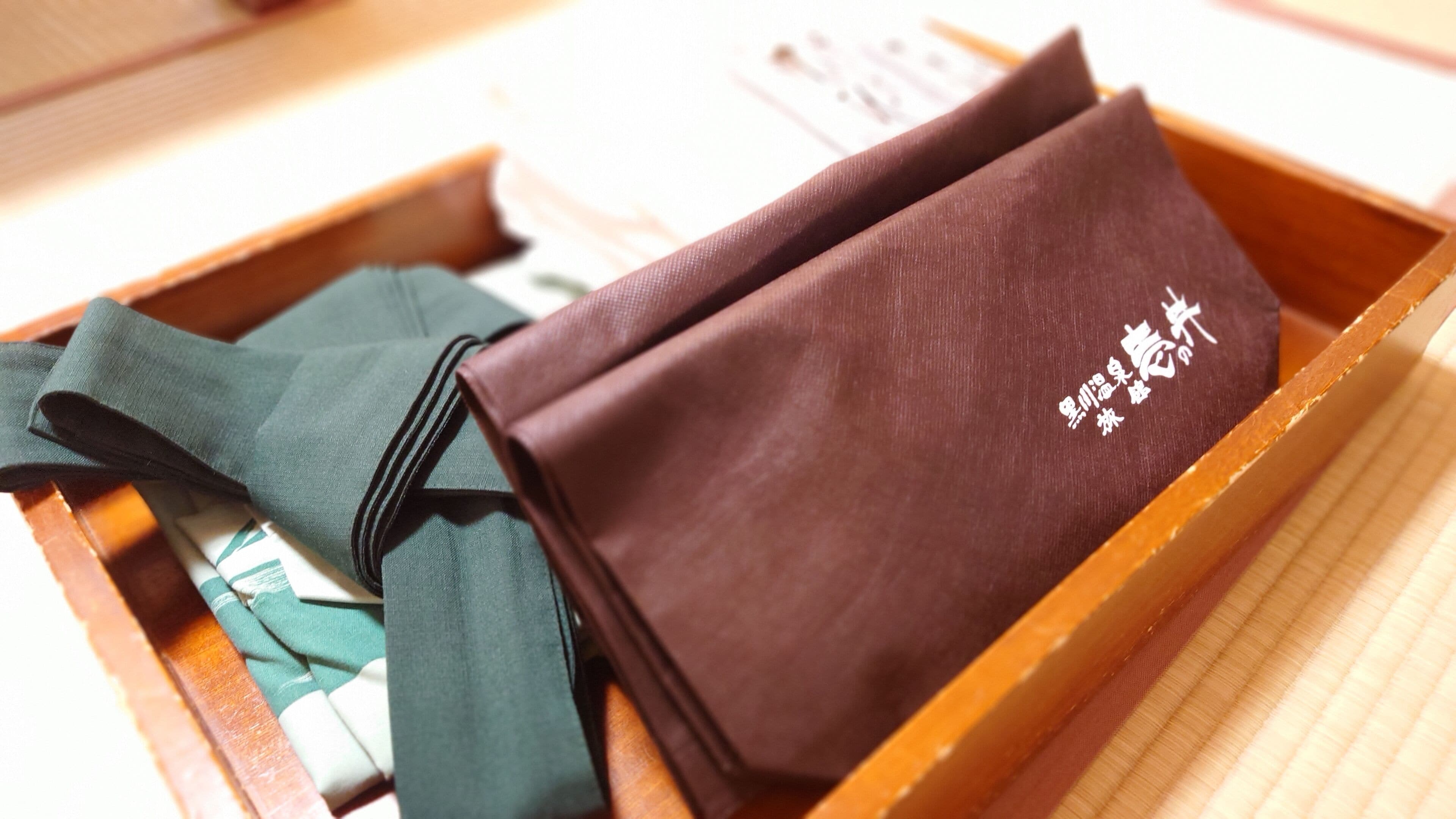 A wooden tray with folded fabric items, including a dark brown piece with white text and a green piece with a white stripe.