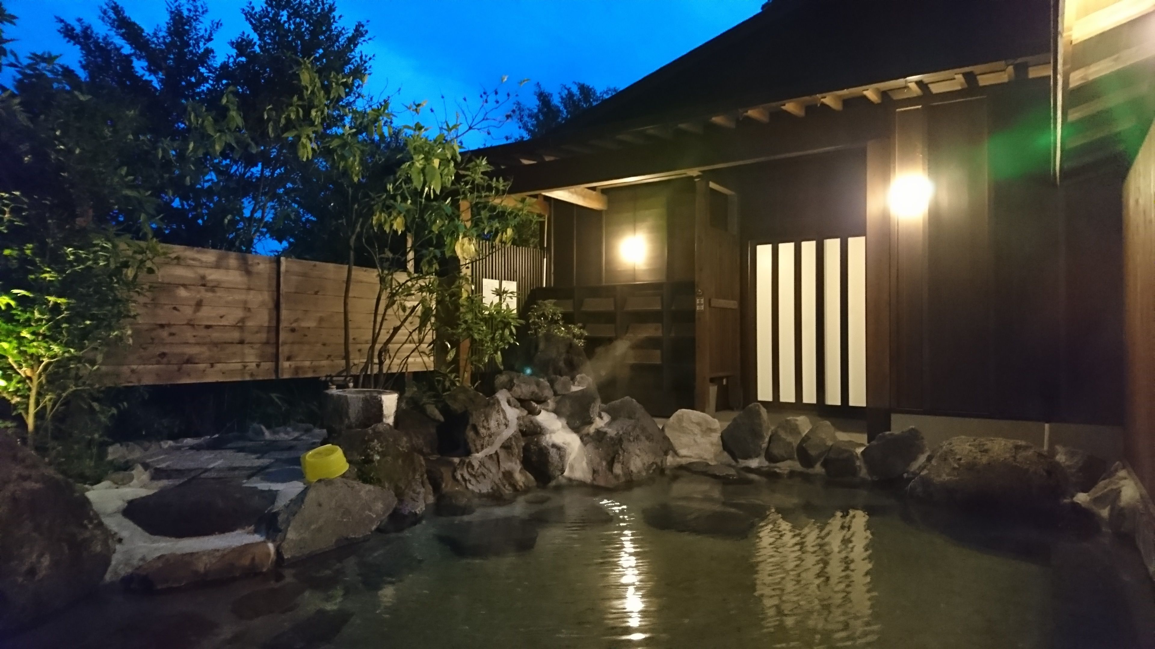 A traditional Japanese garden with a koi pond, wooden bridge, and a building with sliding doors.