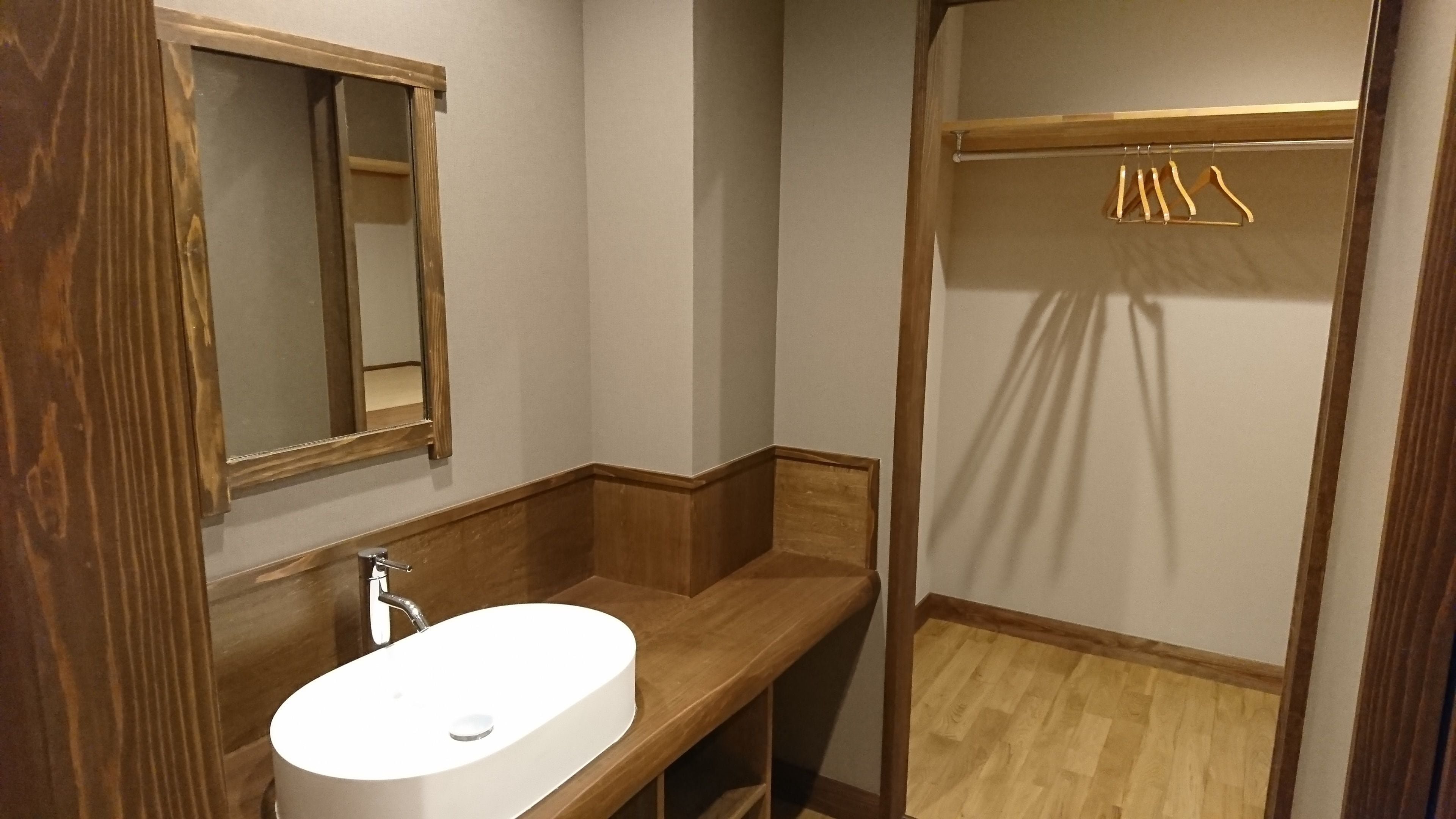 A bathroom with a wooden vanity, a white sink, a mirror, and a shower area with wooden flooring.