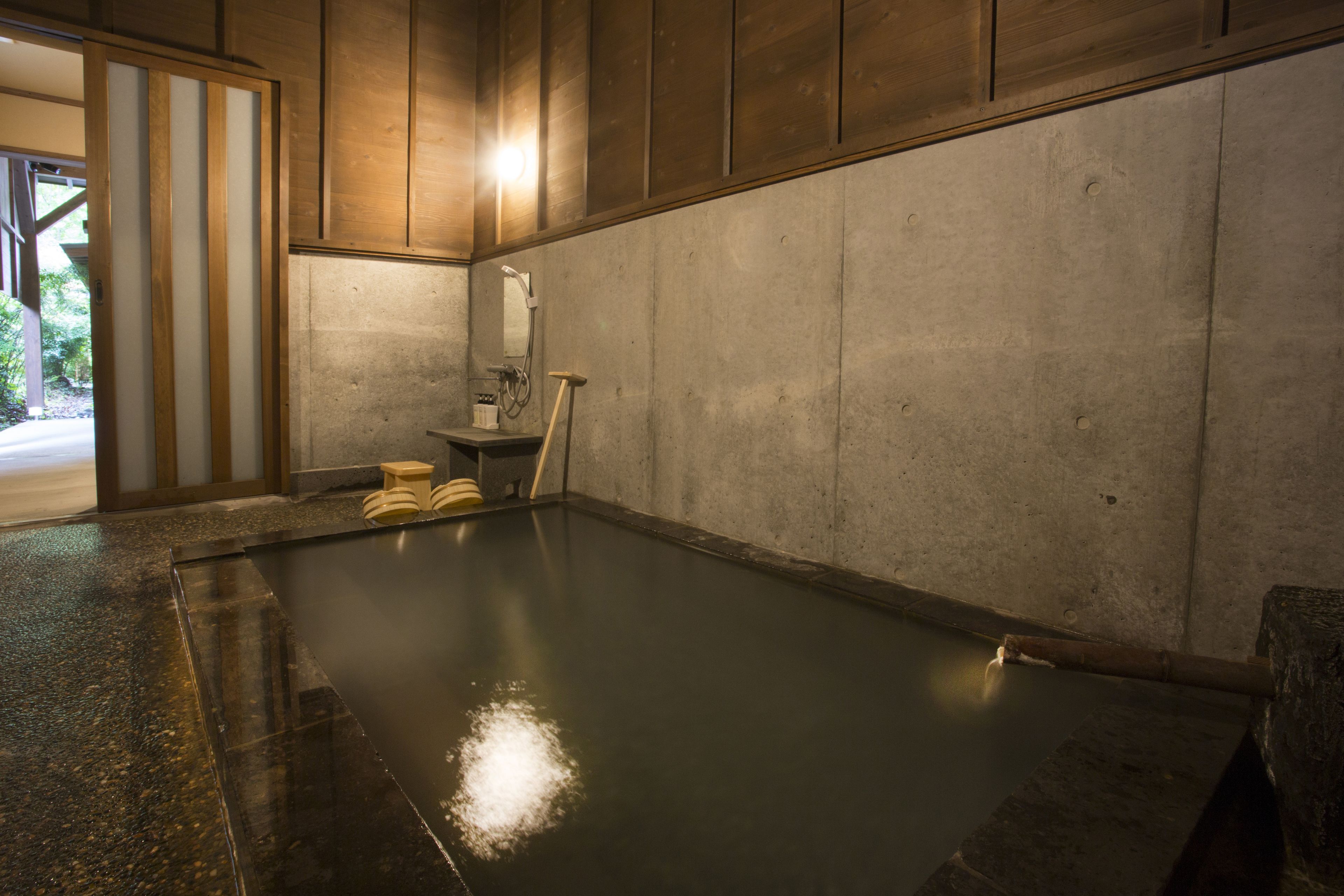 Zona de spa con una bañera de hidromasaje, taburetes de madera y una pared de piedra.