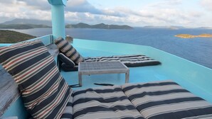 Un balcone con cuscini a righe e un piccolo tavolo, con vista su uno specchio d'acqua e isole in lontananza.