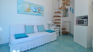 Ein Schlafzimmer mit einem weißen Bett, türkisfarbenen Kissen, einem Gemälde an der Wand, einer Treppe und einer Mikrowelle in der Küchenzeile.