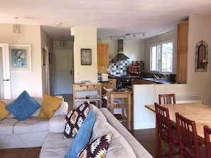 Ein Wohnzimmer mit einer Couch, einem Esstisch und Stühlen. Es gibt eine Küchenzeile mit Herd, Spüle und Schränken.