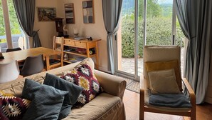 A cozy room with a sofa, a wooden desk, and a chair. There are curtains, a window with a view of greenery, and a painting on the wall. - Secluded villa with large garden pool
Overlooks beautiful picturesque
village (Soubès)