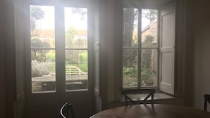 A room with a round table and two chairs, large windows with a view of a garden and a fence.