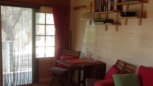 A cozy cabin interior with a wooden dining table, red sofa, and a bookshelf filled with books and decorative items. - An off-grid cabin for two, with views of the Els Ports Mountain range   (Tivenys)