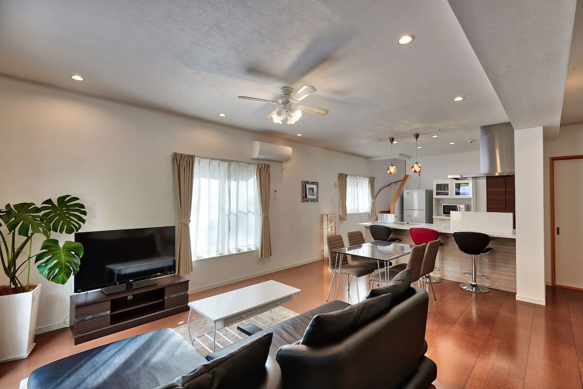 A modern living room with a flat-screen TV, a ceiling fan, and a dining area with a table and chairs.
