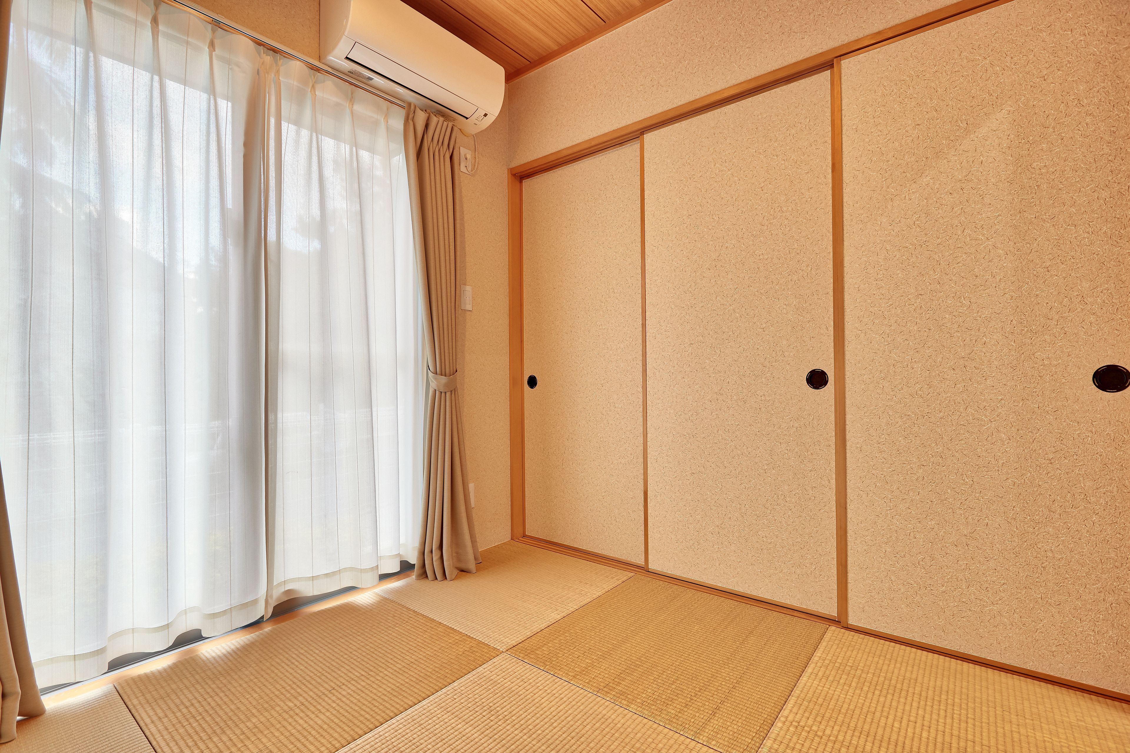 A room with tatami flooring, sliding doors, and a window with sheer curtains.