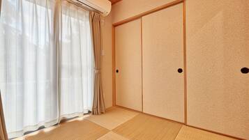 A room with tatami flooring, sliding doors, and a window with sheer curtains.