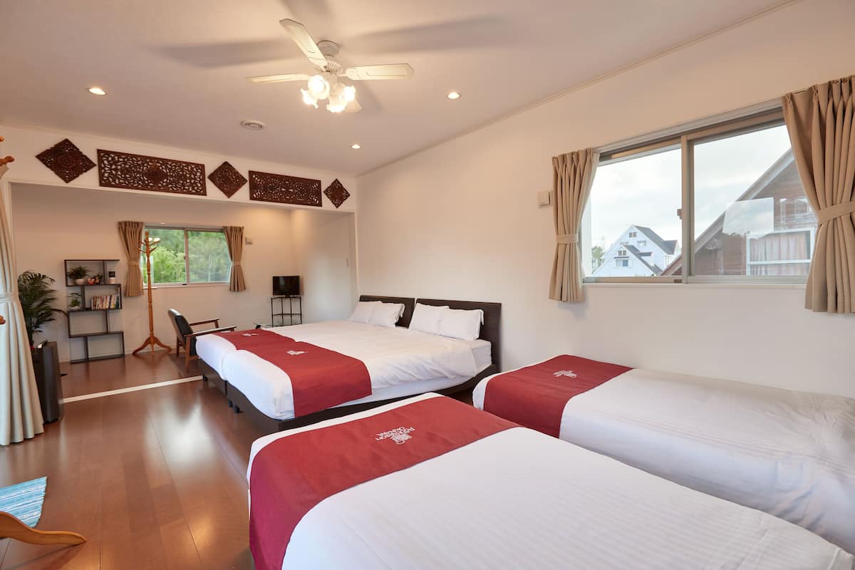 A hotel room with two beds, a desk, a chair, a ceiling fan, and a window with curtains.